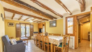Uma sala de jantar com mesa e cadeiras de madeira, um sofá e uma televisão.