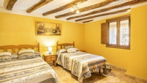 Quarto com duas camas, um quadro na parede, janela com cortinas e vigas de madeira aparente no teto.