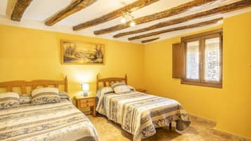 A room with two beds, a painting on the wall, a window with curtains, and exposed wooden beams on the ceiling.
