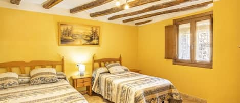 Una habitación con dos camas, un cuadro en la pared, una ventana con cortinas y vigas de madera a la vista en el techo.