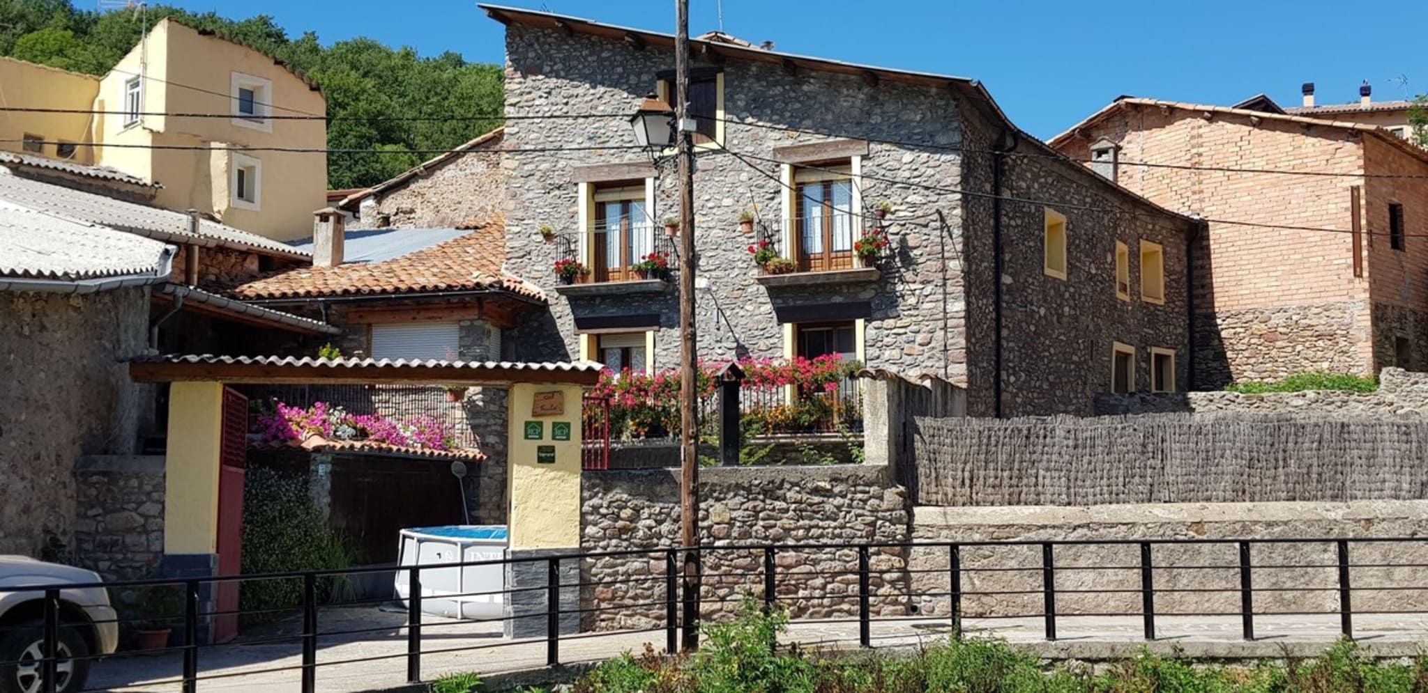 Un edificio de piedra con un balcón, una pequeña tienda con toldo amarillo y una cerca de metal al frente.
