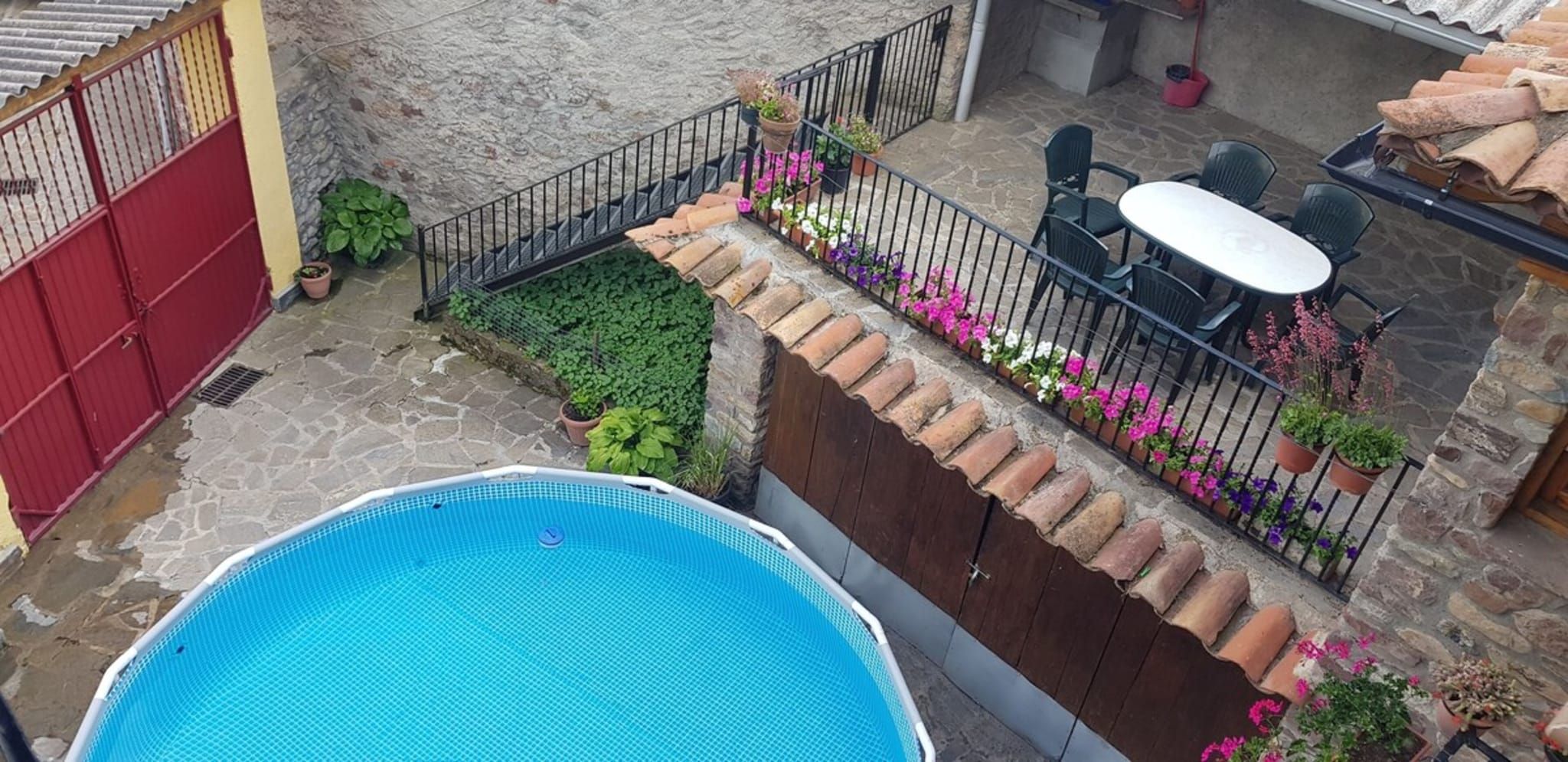 A swimming pool with a tiled deck, a patio area with outdoor furniture, and a stone wall.
