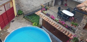 A swimming pool with a tiled deck, a patio area with outdoor furniture, and a stone wall.