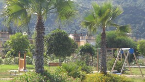 A park with palm trees, playground equipment, and a building in the background.