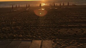 A beach with umbrellas and lounge chairs arranged in rows, facing the ocean.