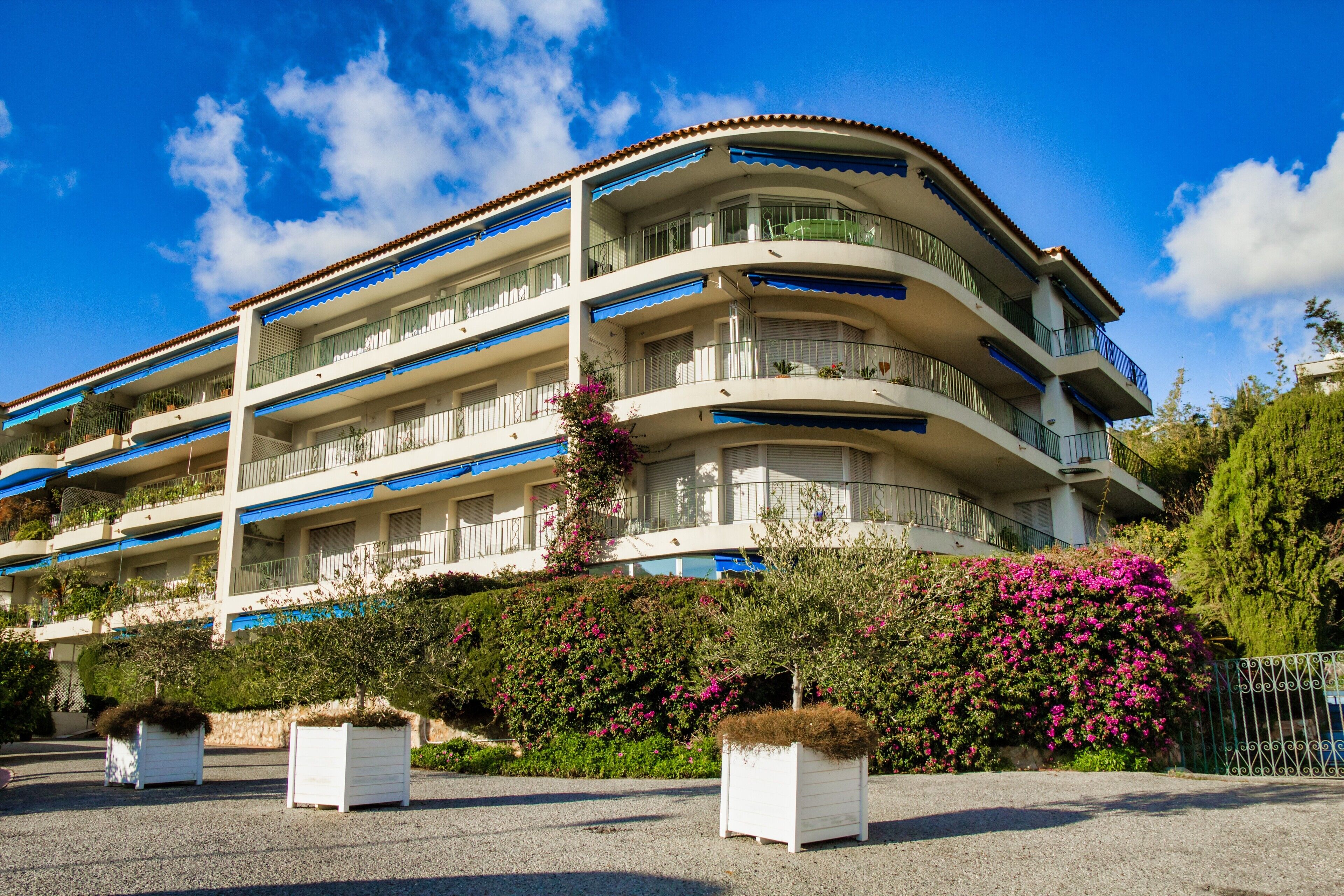 Een meerlaags hotel met balkons, een tuin met potplanten en een helderblauwe lucht.