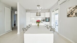 Una cocina moderna con armarios blancos, una isla central con un jarrón de flores y un comedor con sillas.