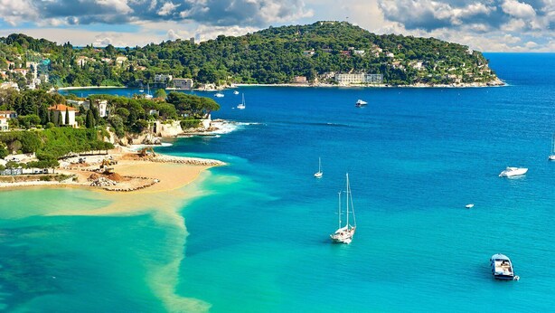 Un pueblo costero con playa, barcos y edificios en una colina.