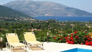 A pool area with lounge chairs and a view of a coastal town and mountains. - Modern comfortable villa with private pool and stunning view (Tzanetata)