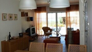 A spacious living area with a dining table, chairs, a sofa, and a TV. There are large windows with curtains, a wooden cabinet, and framed pictures on the wall. - Modern comfortable villa with private pool and stunning view (Tzanetata)