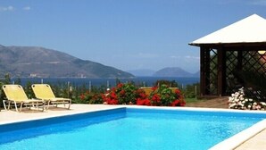 A swimming pool with two yellow lounge chairs, surrounded by red flowers, and a gazebo with a white roof. - Modern comfortable villa with private pool and stunning view (Tzanetata)