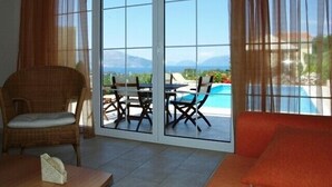 A room with a view of a pool and mountains, featuring a wicker chair, a table, and a sofa. - Modern comfortable villa with private pool and stunning view (Tzanetata)