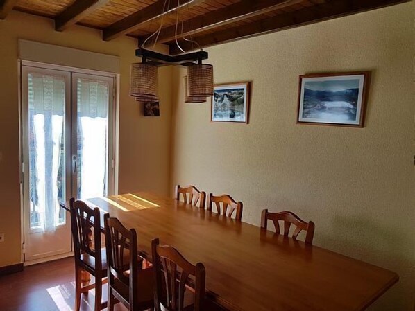 Un comedor con mesa y sillas de madera, techo con vigas a la vista y dos cuadros en la pared.