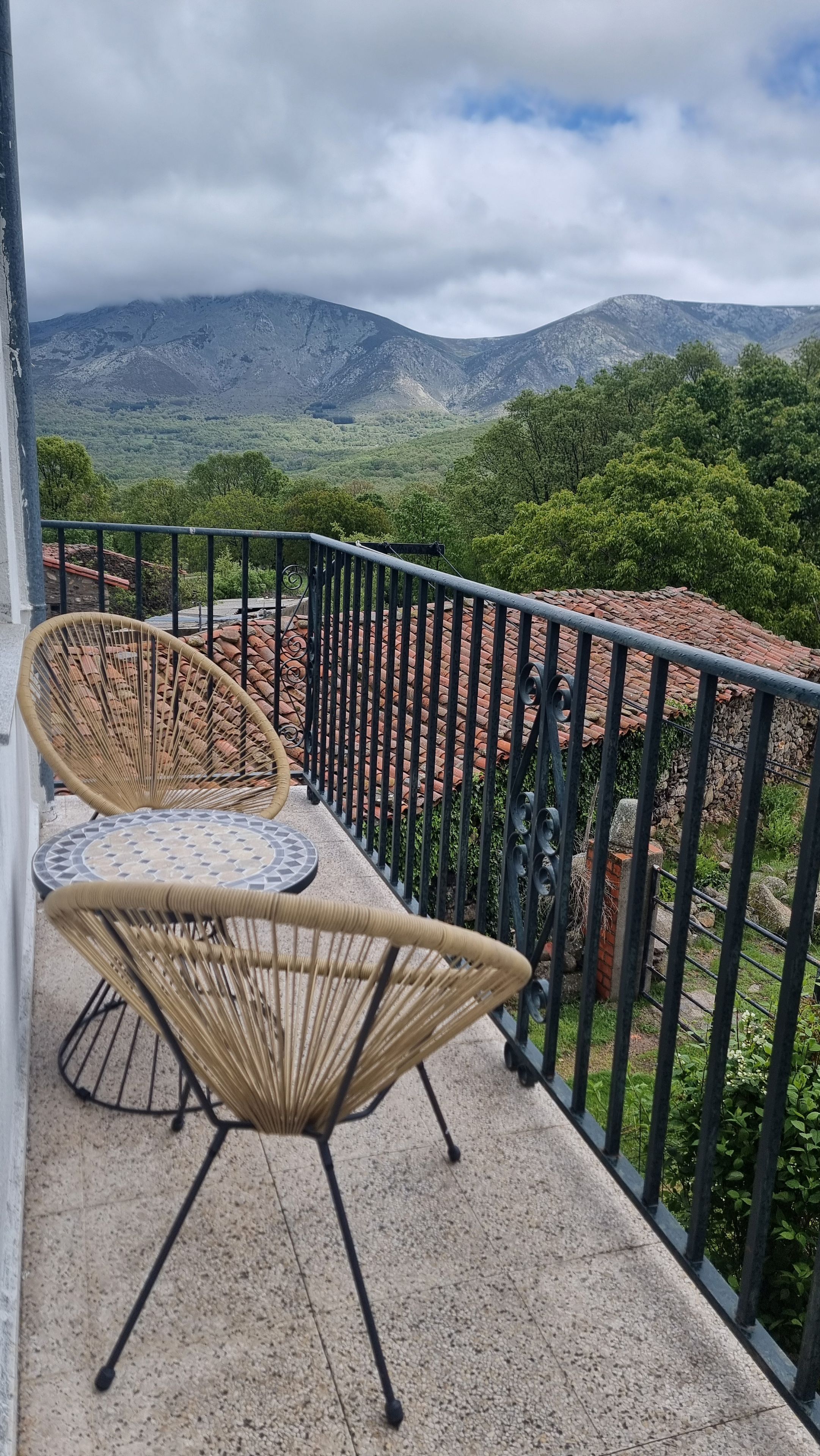 Un balcon avec deux fauteuils en osier et une petite table, offrant une vue sur un paysage montagneux.
