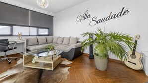 Una sala moderna con un sofá, una mesa de centro de vidrio, una planta en maceta, una guitarra y una pared con el texto 