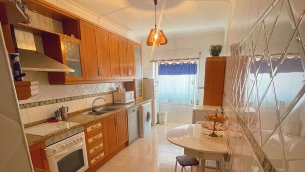 Una cocina con gabinetes de madera, estufa, fregadero y un comedor con mesa y sillas.