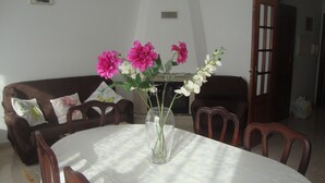 Una mesa de comedor con un florero, rodeada de sillas de madera, en una habitación con un sofá marrón y una chimenea.