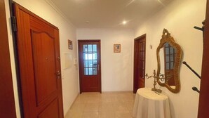 Un pasillo con una puerta de madera, una ventana, una mesa redonda con mantel blanco y un espejo en la pared.
