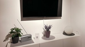 Un soggiorno moderno con una TV a schermo piatto montata a parete, un tavolino con un altoparlante, una pianta in vaso e una sfera decorativa.