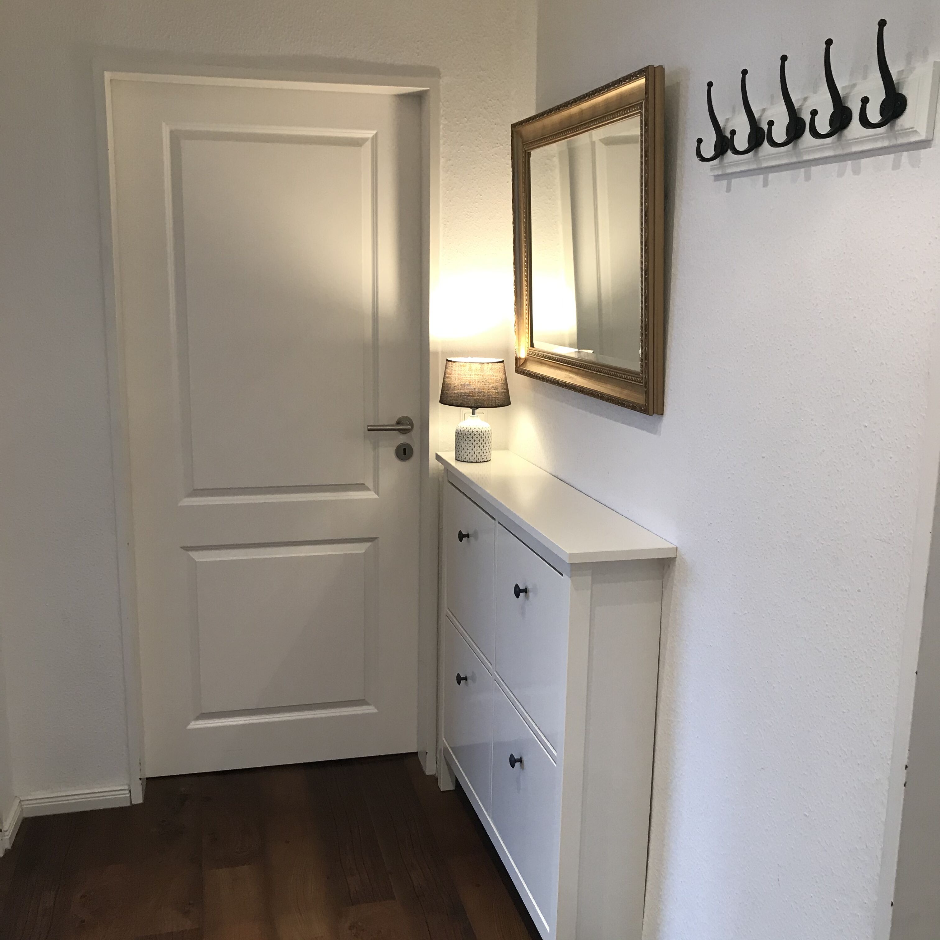 A white door with a handle, a white dresser with drawers, a lamp, and a mirror with a gold frame.