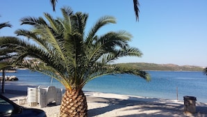 Een strand met een palmboom, witte plastic stoelen en een heldere blauwe zee.