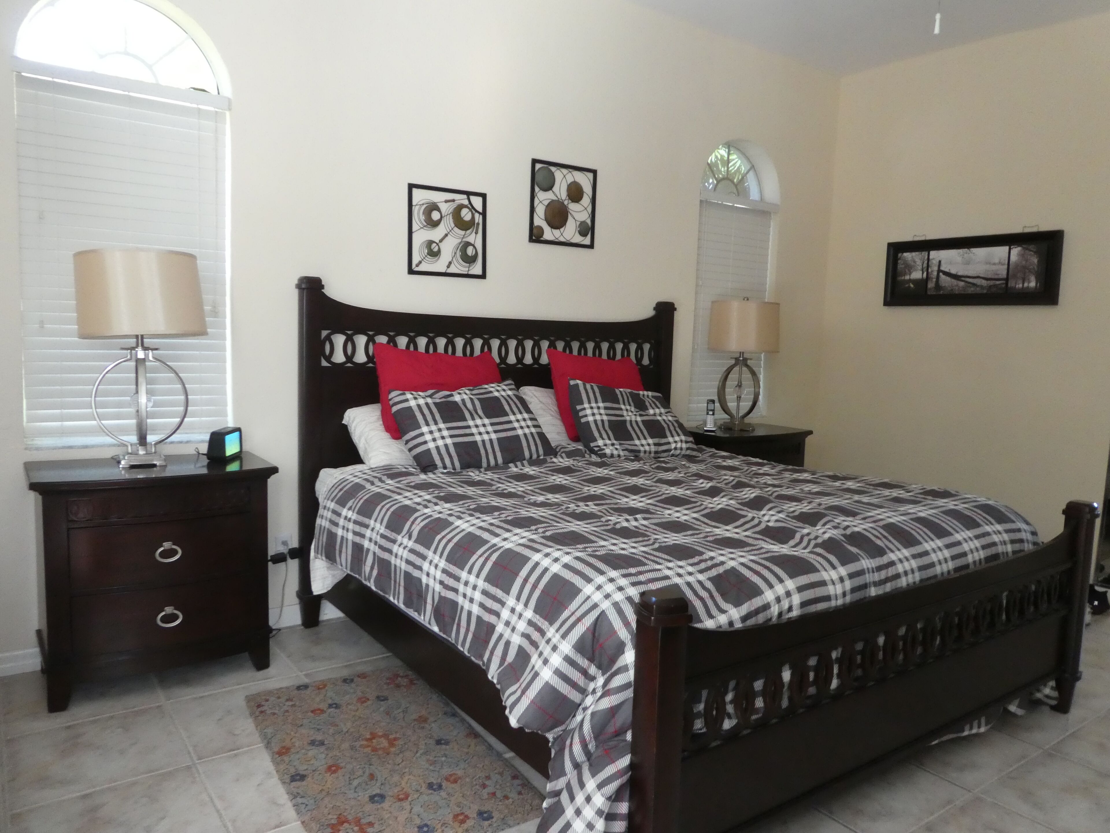 A bedroom with a bed, two bedside tables, a nightstand, a window with blinds, and two wall-mounted lamps.