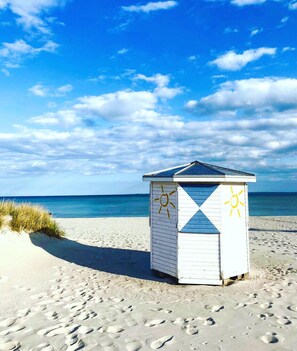 A beach hut with a simple design, featuring a sun symbol on its side, located on a sandy beach with footprints leading up to it. - Feel-good apartment StrandGut für Ostseegenießer, Hs. Atlantic (Grömitz)