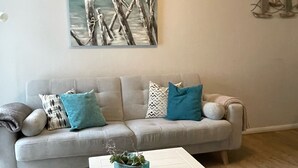 A living room with a grey sofa, teal and white pillows, a coffee table with a plant, and a painting of a beach scene on the wall. - Feel-good apartment StrandGut für Ostseegenießer, Hs. Atlantic (Grömitz)