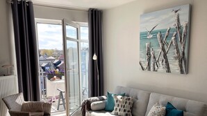 A living room with a sofa, a coffee table, a chair, and a painting of a seascape. - Feel-good apartment StrandGut für Ostseegenießer, Hs. Atlantic (Grömitz)