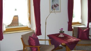 A room with a dining table, two chairs, a floor lamp, and a window with curtains.