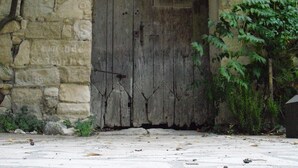 Un edificio de piedra con una gran puerta de madera, rodeado de follaje y suelo empedrado.