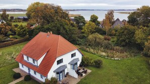 A two-story house with a red-tiled roof, a white exterior, and a small patio with outdoor furniture. - Comfortable holiday house for 7 persons with sauna, 110 sqm, in the south of Rügen (Zudar/Rügen)