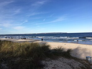 Una playa con gente caminando por la orilla, cielo despejado y el océano al fondo.