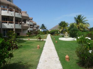 Stroll along the resort's central pathway to a building with multiple balconies, surrounded by lush gardens and palm trees.