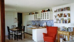 Een moderne keuken met witte kasten, een centraal eiland en een eethoek met een rode stoel.
