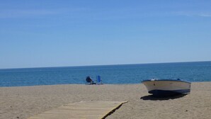 A beach with a wooden walkway leading to the water, a boat on the sand, and a clear blue sky. - Luxury penthouse with stunning views of the sea and golf course (Mijas)