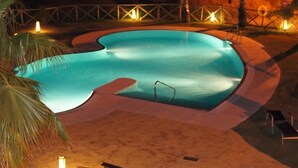 A swimming pool with a curved edge, surrounded by a sandy area and palm trees. - Luxury penthouse with stunning views of the sea and golf course (Mijas)