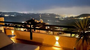 A terrace with a view of a city at night, including a pool area and a potted plant. - Luxury penthouse with stunning views of the sea and golf course (Mijas)