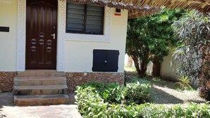 A house with a thatched roof, a stone staircase leading to a wooden door, and a small garden with various plants. - Villa LeoMar: Exclusive vacation home with pool & garden, 350 m from the beach (Diani Beach)