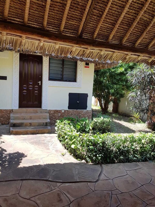 Una casa con techo de paja, una escalera de piedra que lleva a una puerta de madera y un pequeño jardín con diversas plantas.