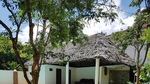 A swimming pool with a thatched roof structure, surrounded by a grassy lawn and trees. - Villa LeoMar: Exclusive vacation home with pool & garden, 350 m from the beach (Diani Beach)