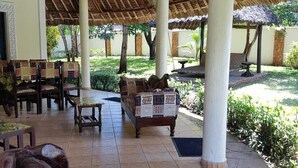 An outdoor covered area with tiled flooring, wooden furniture, and a decorative elephant sculpture. - Villa LeoMar: Exclusive vacation home with pool & garden, 350 m from the beach (Diani Beach)