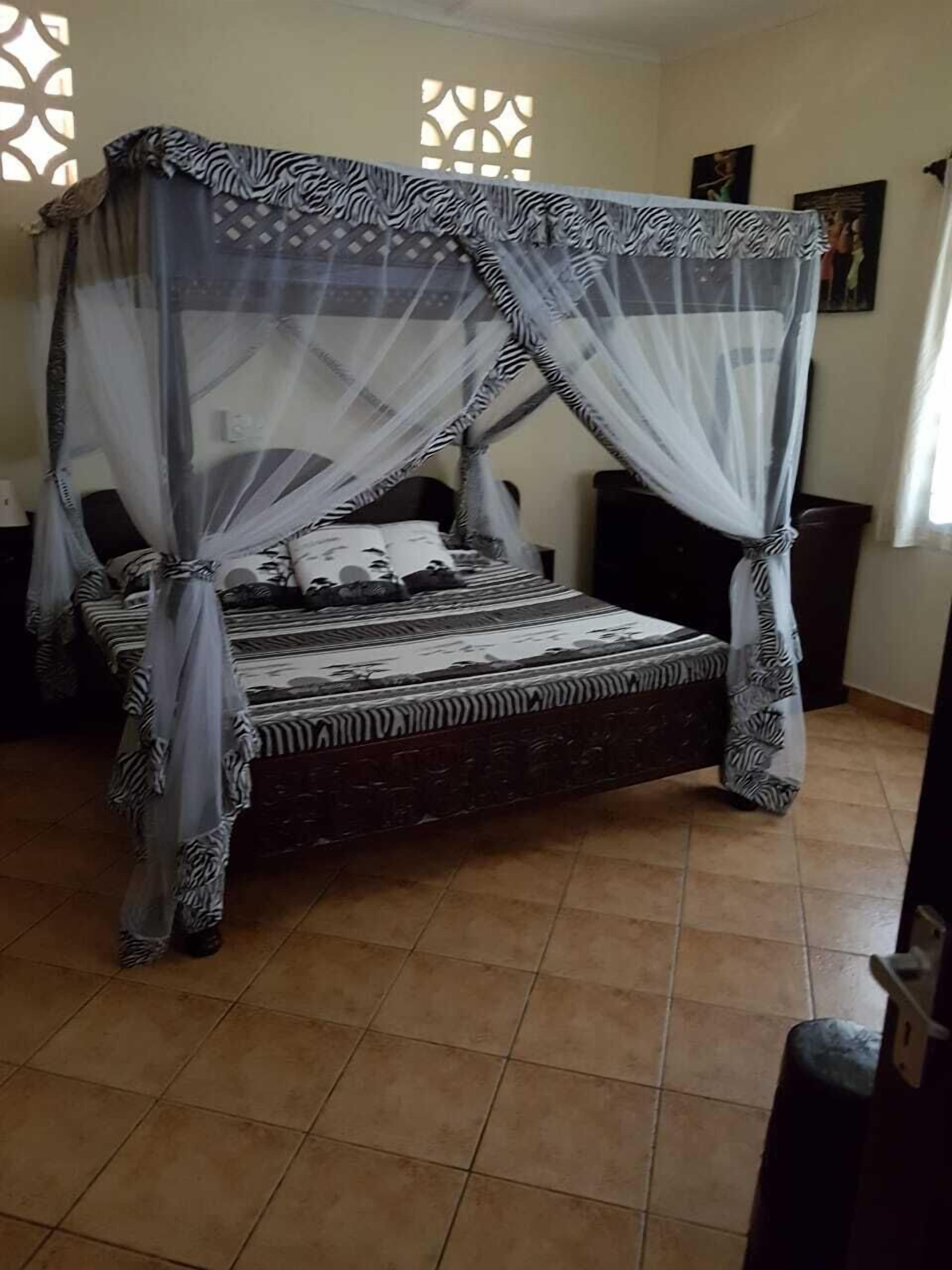 A four-poster bed with a zebra-striped bedspread, a canopy with a zebra pattern, and a tiled floor.