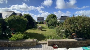 Une terrasse en bois avec des murs en pierre, une cour verdoyante et un ciel bleu dégagé parsemé de nuages.