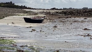 Un bateau sur une plage rocheuse, sous un ciel dégagé.
