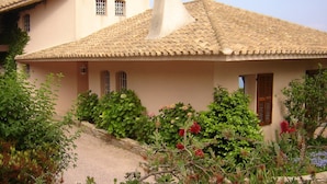 Una casa de dos pisos con techo de tejas, una chimenea y un jardín con diversas plantas y flores.