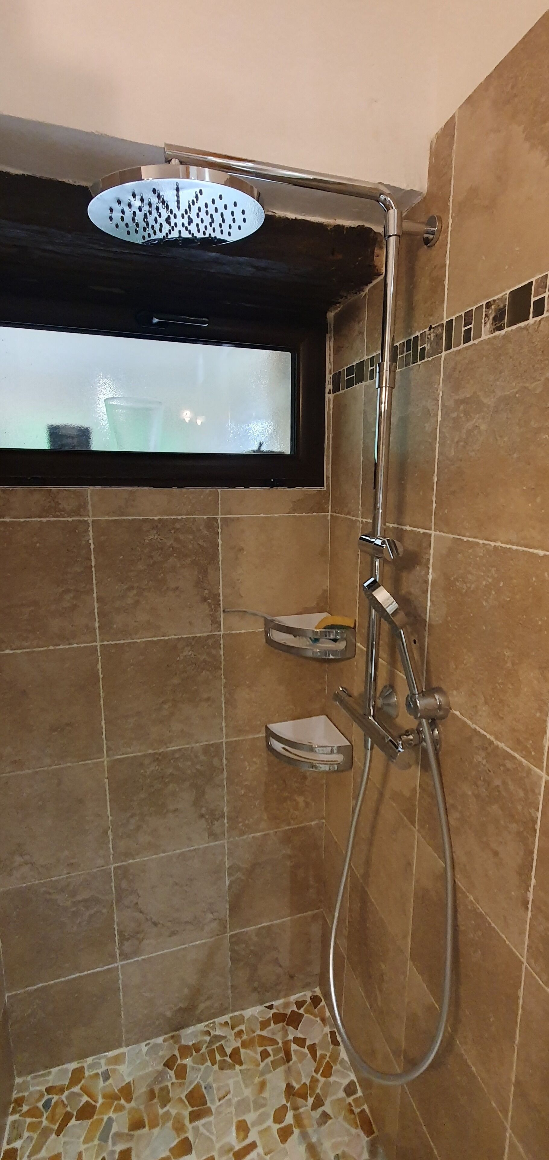Un espacio de ducha con mampara de vidrio, ventana y paredes de azulejos.