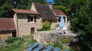 Une maison en pierre avec une piscine, des chaises longues et une table de patio.