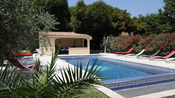 Une piscine bordée de carreaux, entourée de palmiers et de chaises longues rouges.