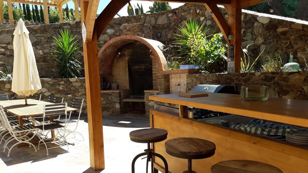An outdoor patio with a stone wall, a wooden pergola, a brick oven, and a bar area with stools. - A FEW STEPS FROM THE SEA, MAS DES PORTALS CRIQUES MAGNIFICENT VIEW, (COLLIOURE)
